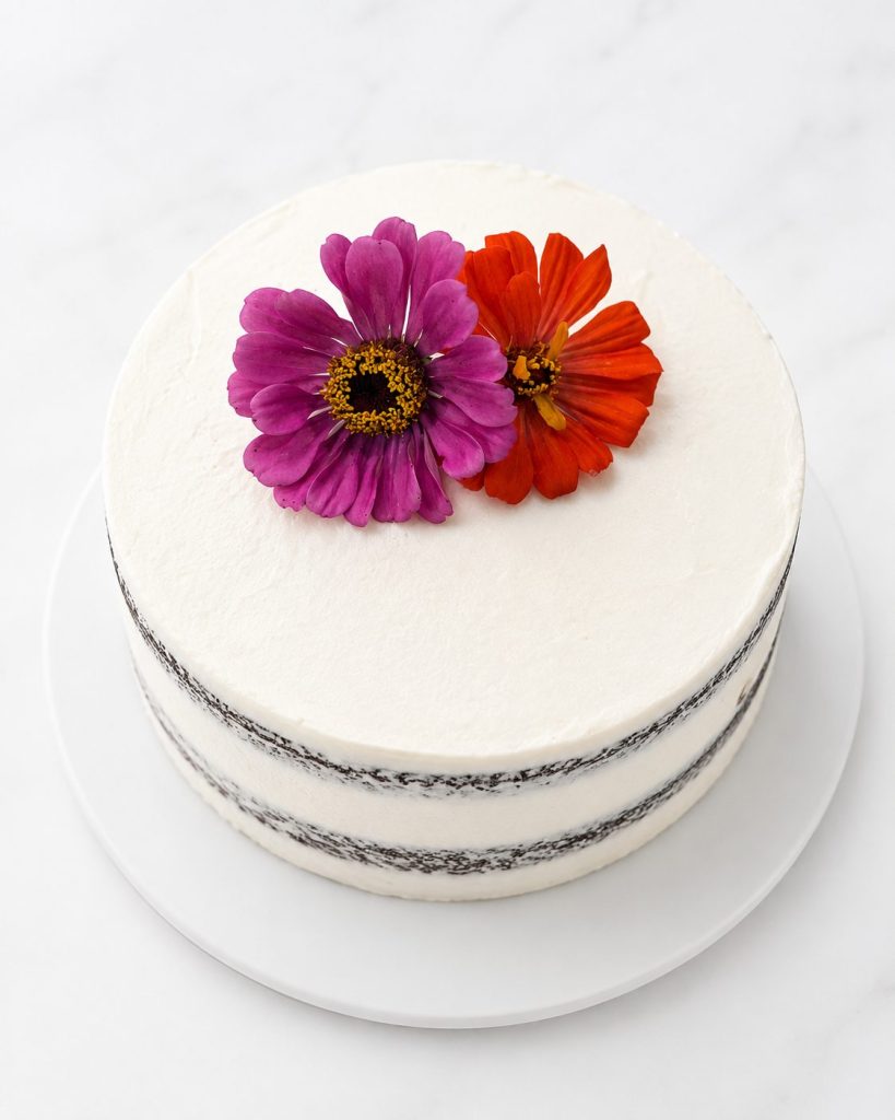 A smooth white cake finished with bright pink and orange zinnias