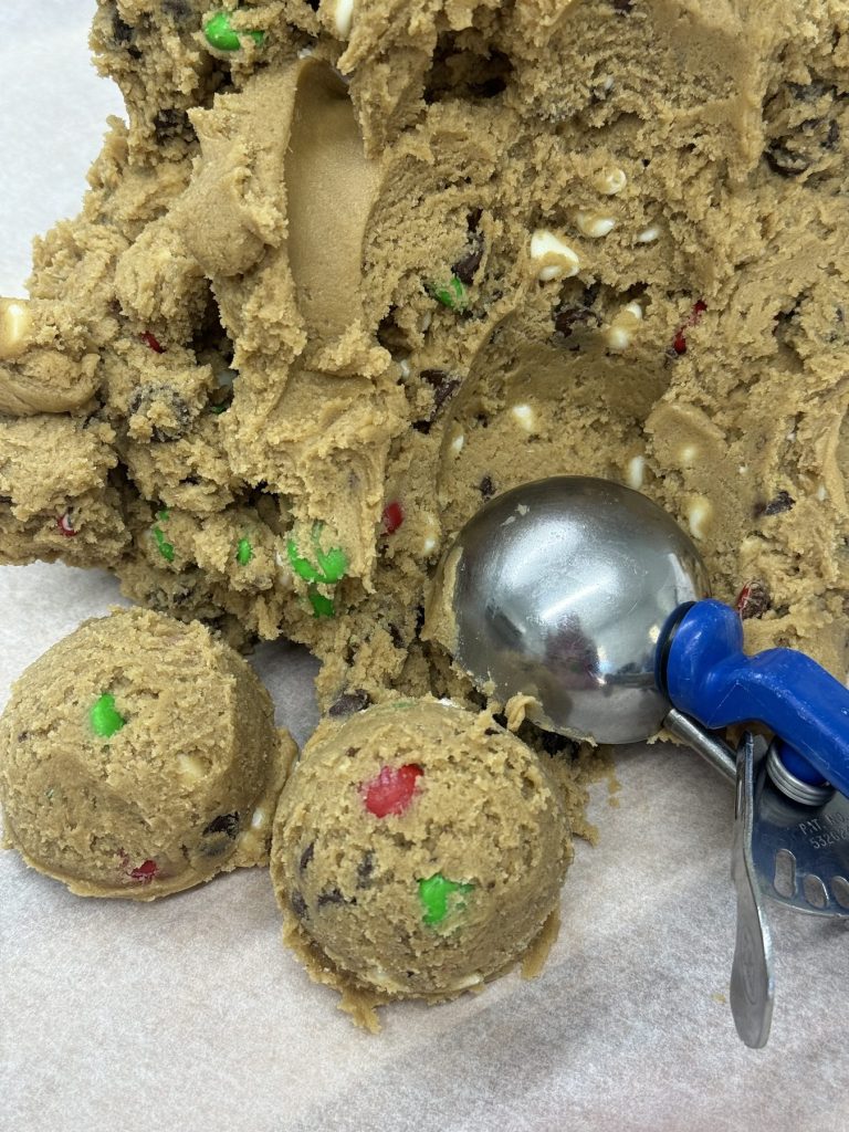 Cookie dough studded with candy pieces being portioned with a scoop