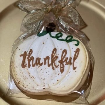 A pumpkin-shaped sugar cookie hand-lettered with the word thankful