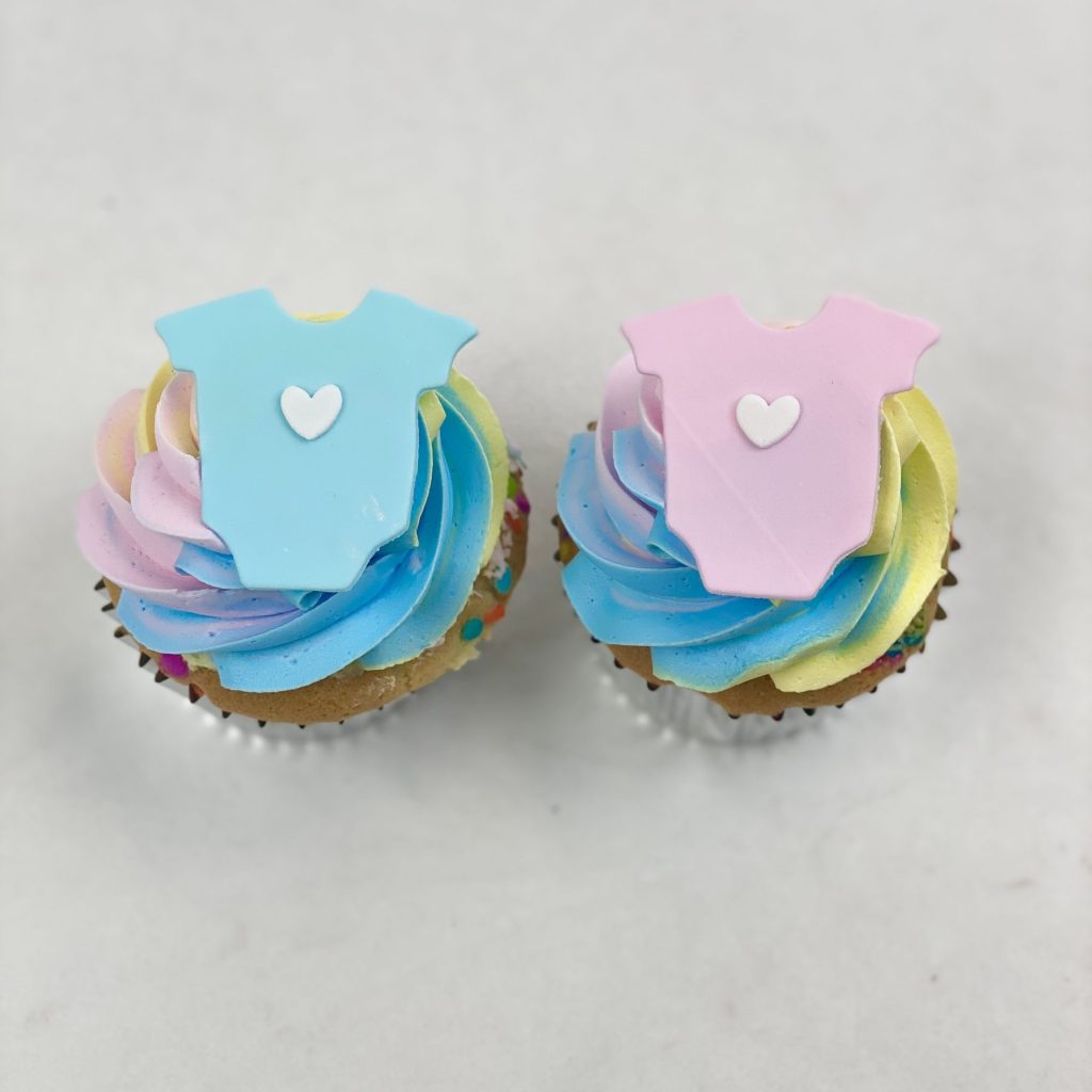 Baby shower cupcakes topped with pink and blue fondant onesies
