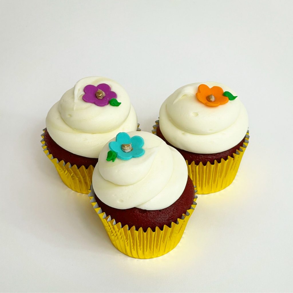 Three cupcakes swirled with white buttercream and topped with sugar flowers