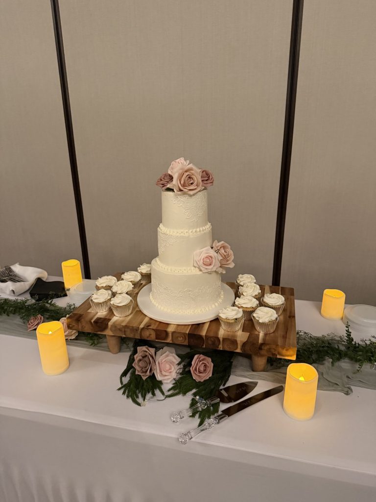 A tiered wedding cake displayed on a wood riser with candles and greenery