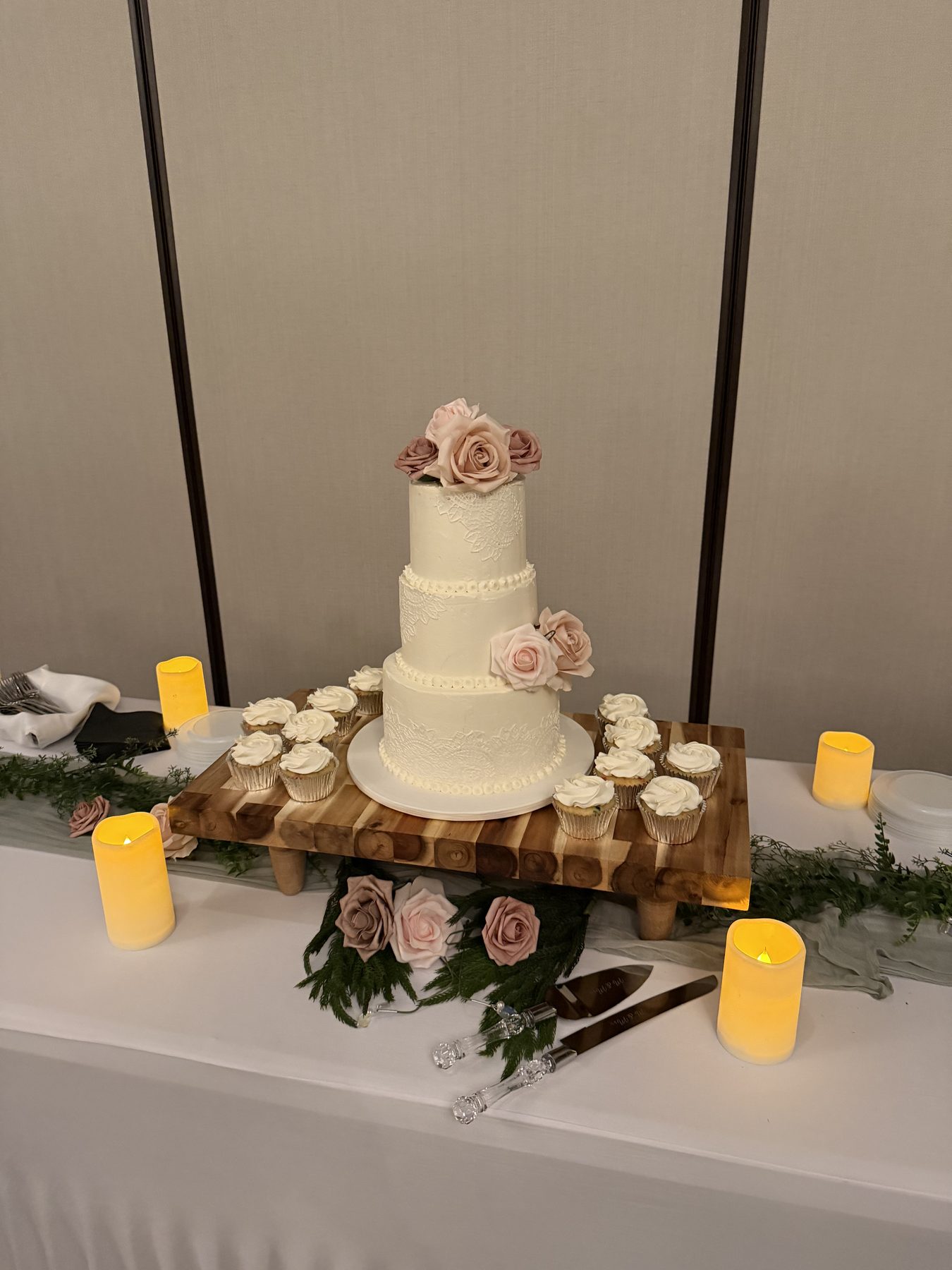 A tiered wedding cake displayed on a wood riser with candles and greenery