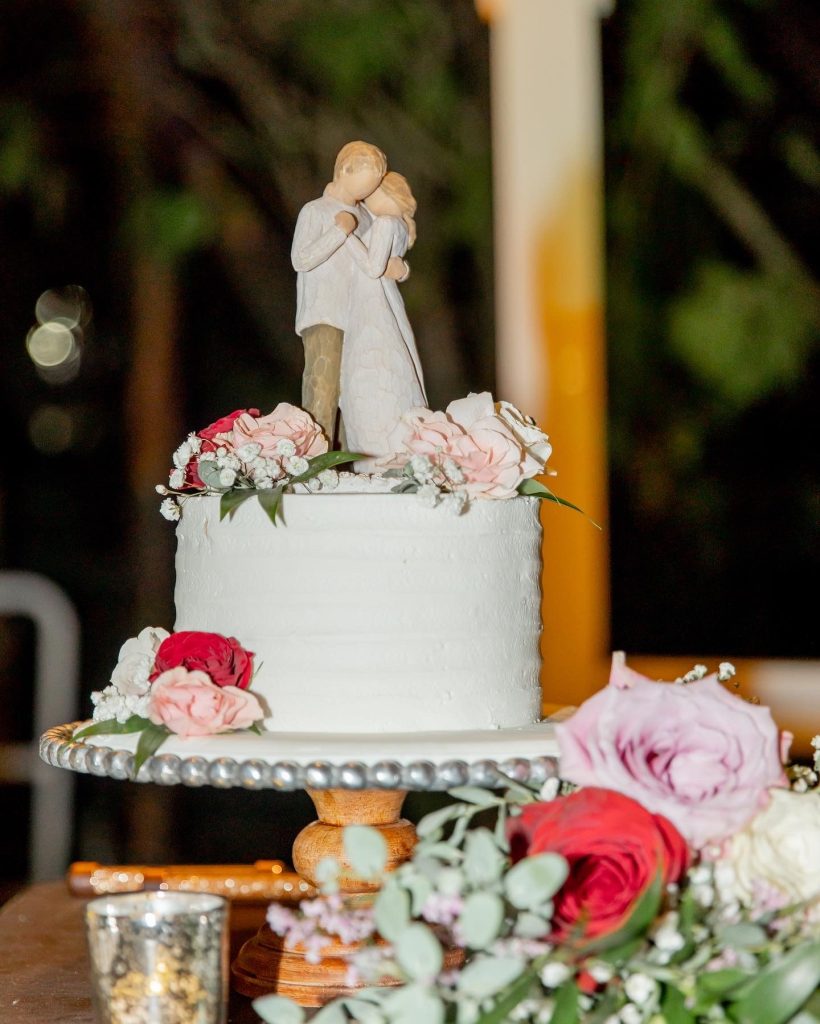 A white wedding cake with a bride and groom topper surrounded by roses